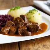 Un plat appétissant de daube de sanglier au vin blanc, servi avec des quenelles et du chou rouge.