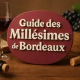 Guide des Millésimes de Bordeaux : un verre de vin rouge, une bouteille, un livre ouvert, des raisins noirs et des bouchons sur une table en bois.