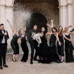 Un groupe joyeux célèbre un mariage noir et blanc, le marié aspergeant de champagne ses demoiselles d'honneur en robe noire.