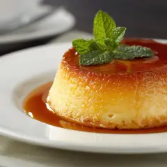 Crème caramel on a white plate, its glossy caramel brûlé toxique topping glistening, garnished with fresh mint.