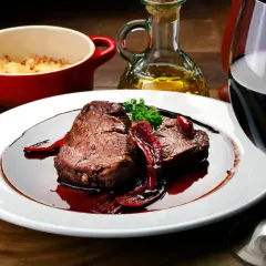Un plat de viande rouge en sauce, accompagné d'une purée gratinée et d'un verre de vin. Parfait pour savoir que manger avec un sancerre rouge.