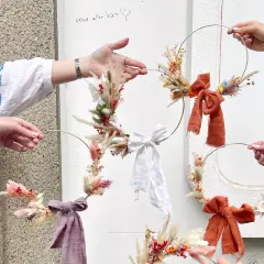 Des mains créatives assemblent des couronnes de fleurs séchées lors d'un atelier EVJF. Ambiance bohème et festive.