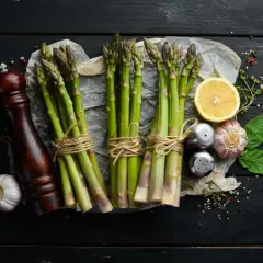 Des asperges fraîches, citron, ail et moulin à poivre sur fond noir. Idéal pour savoir quel vin avec asperges.