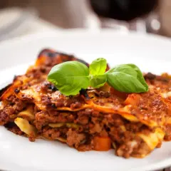 Une part de lasagnes à la bolognaise, garnie de basilic frais. Un plat réconfortant, parfait avec un verre de vin rouge. Quel vin avec des lasagnes ?
