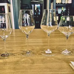 Six verres à vin vides alignés sur un comptoir de bar en bois, prêts pour une dégustation.