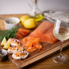 Un verre de vin blanc, parfait pour accompagner le saumon fumé, est présenté avec des toasts, des câpres, des oignons rouges et du citron.