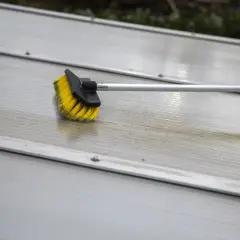 Brosse jaune et noire sur une surface striée en aluminium, en cours de nettoyage.