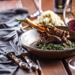 Un plat de vin avec agneau, servi sur un lit d'épinards, avec une branche de romarin. Un verre de vin rouge est à côté.