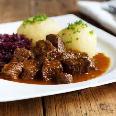 Un plat appétissant de daube de sanglier au vin blanc, servi avec des quenelles et du chou rouge.