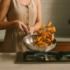 Une personne fait sauter des pommes de terre dans un poêle en inox sur le feu. Attention, le poêle en inox peut être dangereux s'il est mal utilisé.