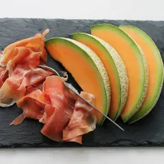 Tranche de melon et jambon cru sur ardoise. Quel vin avec melon et jambon cru ? Un vin blanc sec et fruité ou un rosé léger serait parfait.