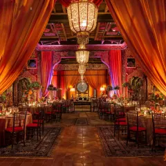 Décoration somptueuse pour un mariage bollywood, avec des drapés orangés, des lustres imposants et des tables dressées dans une ambiance chaleureuse et festive.