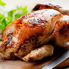 Un délicieux poulet rôti doré sur une planche en bois, prêt à être dégusté. Quel vin avec poulet rôti ? Un blanc fruité ou un rouge léger serait parfait.