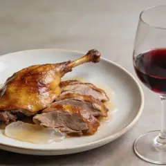 Un plat de canard rôti, tranché et nappé de sauce, accompagné d'un verre de vin rouge. Le parfait accord pour savoir quel vin rouge avec du canard.