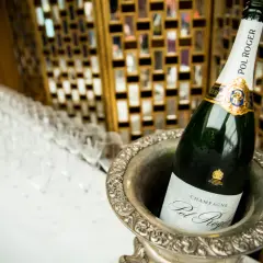 Bouteille de champagne Pol Roger dans un seau à glace, avec des flûtes alignées en arrière-plan.