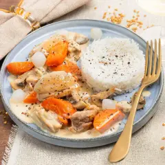 Un plat de dinde à la crème avec carottes, champignons et riz blanc. Un verre de vin blanc à côté.