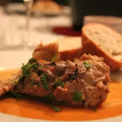 Un plat savoureux de viande mijotée, garni de persil frais, servi avec du pain. Parfait pour accompagner un osso bucco.