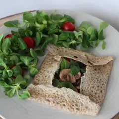 Une galette bretonne garnie de champignons et d'épinards, accompagnée d'une salade verte et de tomates cerises. Un délice pour accompagner un verre de vin.