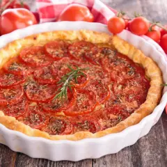 Tarte aux tomates fraîches, garnie d'herbes et d'une branche de romarin. Un accompagnement tarte tomate parfait pour un repas d'été.