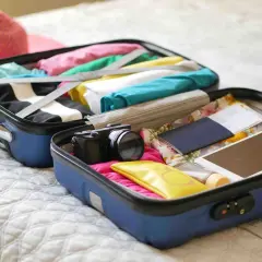 Valise ouverte prête pour un EVJF : vêtements colorés, appareil photo, passeport, tablette. Une liste valise EVJF drôle à compléter !