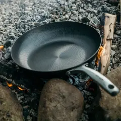 Poêle posée sur des braises et des pierres, prête à redresser le fond d'une poêle pour une cuisson en plein air.