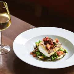 Un verre de vin blanc accompagne un poisson en sauce, servi sur un lit de légumes verts et de courgettes.