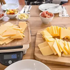 Préparation d'un repas : quelle quantité de fromage pour 40 personnes ? Des tranches de fromage sont coupées sur des planches, avec des accompagnements comme des pommes de terre et des cornichons.
