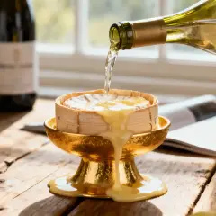 Vin blanc versé sur un fromage fondant, prêt pour une fondue suisse. Raisins et bouteille en arrière-plan.