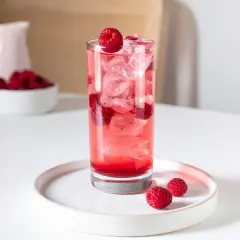 Verre de boisson sans alcool aux framboises, parfait pour accompagner un repas. Glaçons et fruits frais pour une touche rafraîchissante.