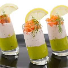 Trois verrines végétariennes colorées, garnies de saumon fumé, d'une crème légère et d'une touche d'aneth, sur une assiette noire.