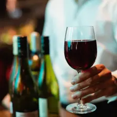 Main tenant d'un verre de bon beaujolais, avec des bouteilles en arrière-plan.