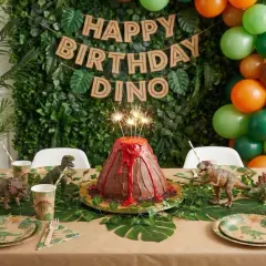 Gâteau volcan et décorations pour une activité anniversaire thème dinosaure. Ballons verts, oranges et bruns. Guirlande "Happy Birthday Dino".