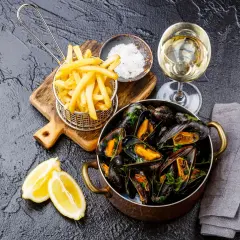 Un plat de moules frites, accompagné de quartiers de citron, d'une coupelle de gros sel et d'un verre de vin blanc.