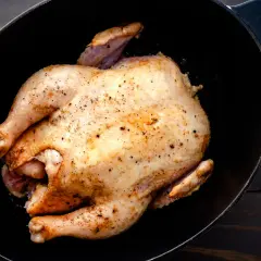 Un poulet rôti doré, assaisonné de poivre, repose dans une cocotte en fonte. Un délice prêt à être dégusté, un vrai poulet Calvi.