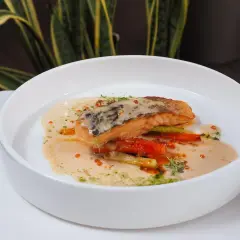 Un filet de poisson poêlé, baignant dans une onctueuse sauce champagne, accompagné de légumes croquants et de quelques perles orangées.