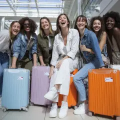 Groupe de femmes joyeuses à l'aéroport avec leurs valises colorées, prêtes pour une destination EVJF pas cher.