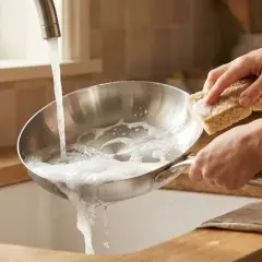 Main tenant, une éponge savonneuse pour nettoyer poêle sous un jet d'eau.