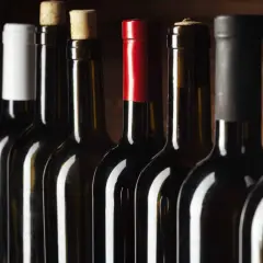 Une rangée de bouteilles de vin sombres, certaines avec des bouchons en liège, d'autres avec des capsules colorées. Un millésime Beaujolais pourrait se cacher parmi elles.