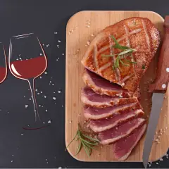 Un plat de magret de canard tranché, garni de romarin, prêt à être dégusté avec deux verres de vin rouge.