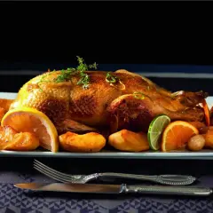 Canard rôti, pommes caramélisées et agrumes en accompagnement. Une canette dorée, prête à être dégustée.