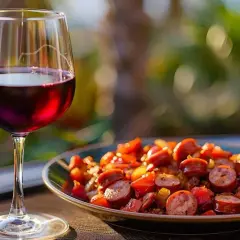 Un verre de vin rouge accompagne un plat de rougail saucisse, aux couleurs vives et appétissantes, sous un soleil doux.