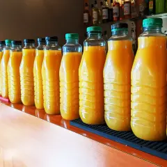 Une longue rangée de bouteilles de jus d'orange, prêtes pour une fête. 5 litres de punch pour combien de personnes ?