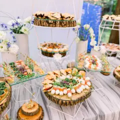 Un buffet de mariage participatif avec une variété de petits fours, tartines et brochettes, joliment présentés sur des rondins de bois et des étagères en verre.