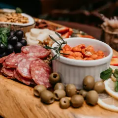 Un buffet campagnard pour 20 personnes : raisins noirs, salami, olives, cacahuètes épicées, citron et menthe sur un plateau en bois.