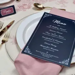 Une table dressée pour un mariage, avec un menu élégant proposant une idée menu mariage original. Couverts dorés, serviette rose poudré.