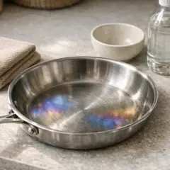 Casserole inox aux reflets irisés, comme des taches bleues, prête pour un nettoyage. À côté, une serviette pliée et un petit bol.