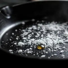 Une cocotte brulée, avec une goutte d'huile dorée au milieu d'une poudre blanche.