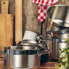 Ustensiles de cuisine en acier inoxydable 18/8, dont une casserole brillante, une théière blanche et des planches à découper en bois.