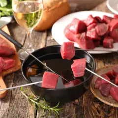 Préparer une fondue bourguignonne : des dés de bœuf crus sur des brochettes, prêts à être plongés dans l'huile chaude. Un verre de vin blanc à côté.