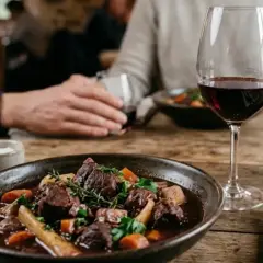 Un plat de sanglier en sauce, garni d'herbes et de légumes, servi avec un verre de vin rouge Cahors. Quel vin avec sanglier en sauce ? Ce Cahors est parfait.